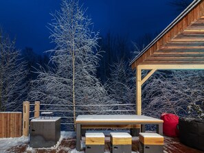 A wooden deck with a table and benches, surrounded by snow-covered trees and a wooden building structure. - Villa in Celadna With Outdoor Cinema & Whirlpool (Celadna)