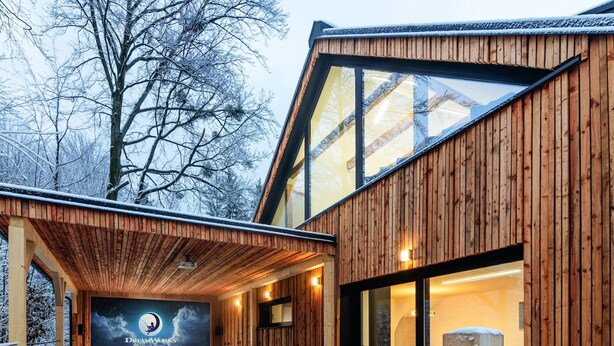 A wooden cabin with a large glass door, a covered outdoor seating area, and a poster on the wall. - Villa in Celadna With Outdoor Cinema & Whirlpool (Celadna)