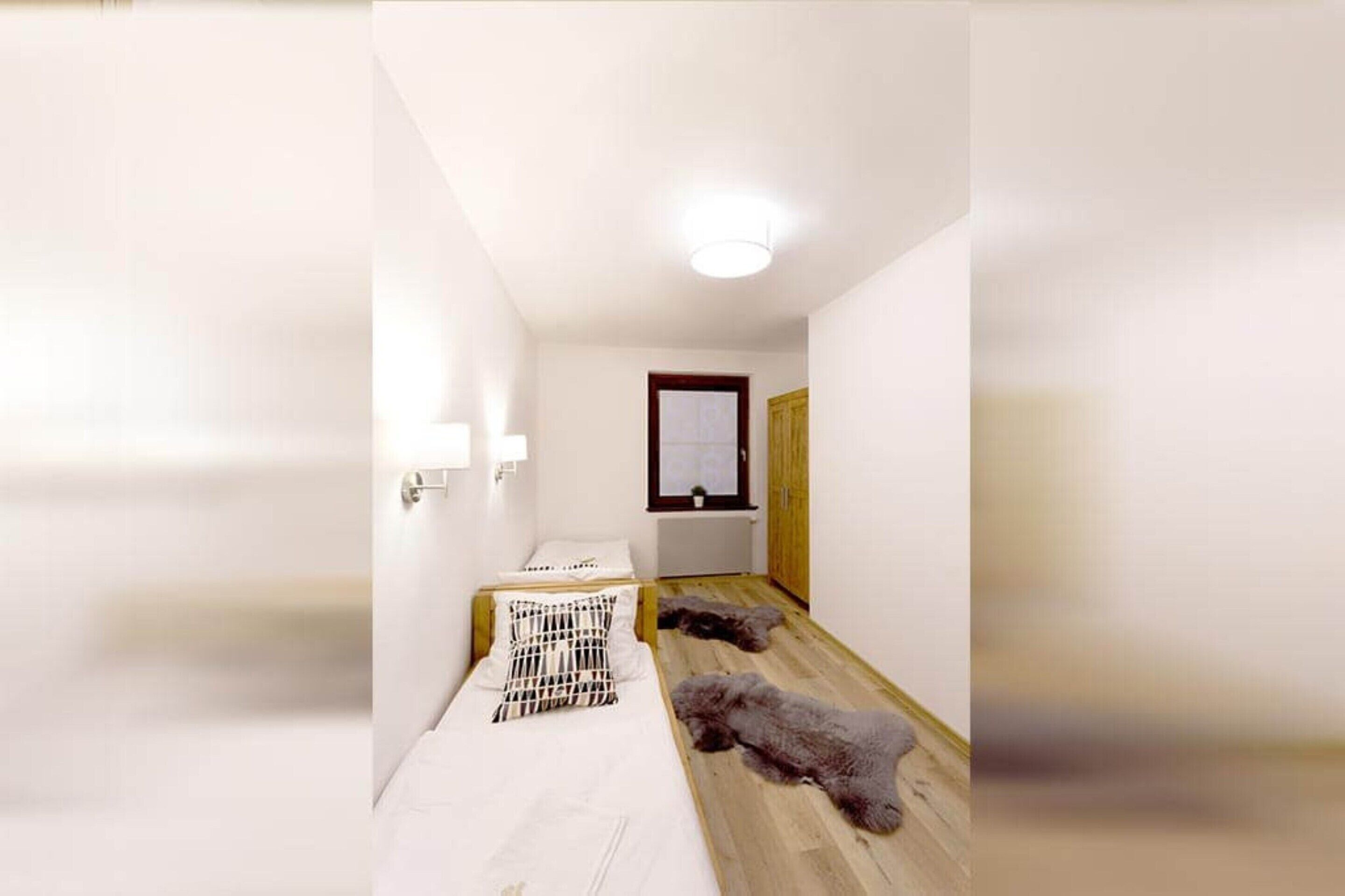 Un couloir étroit, avec un lit sur le côté gauche et une porte en bois au fond.