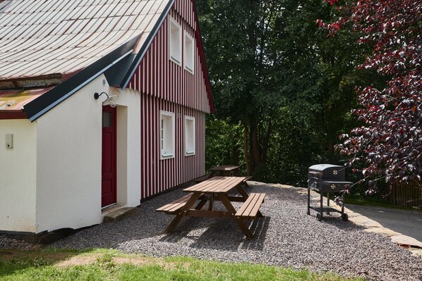 Une table de pique-nique est installée devant un bâtiment dont la porte et les fenêtres sont peintes en rouge.