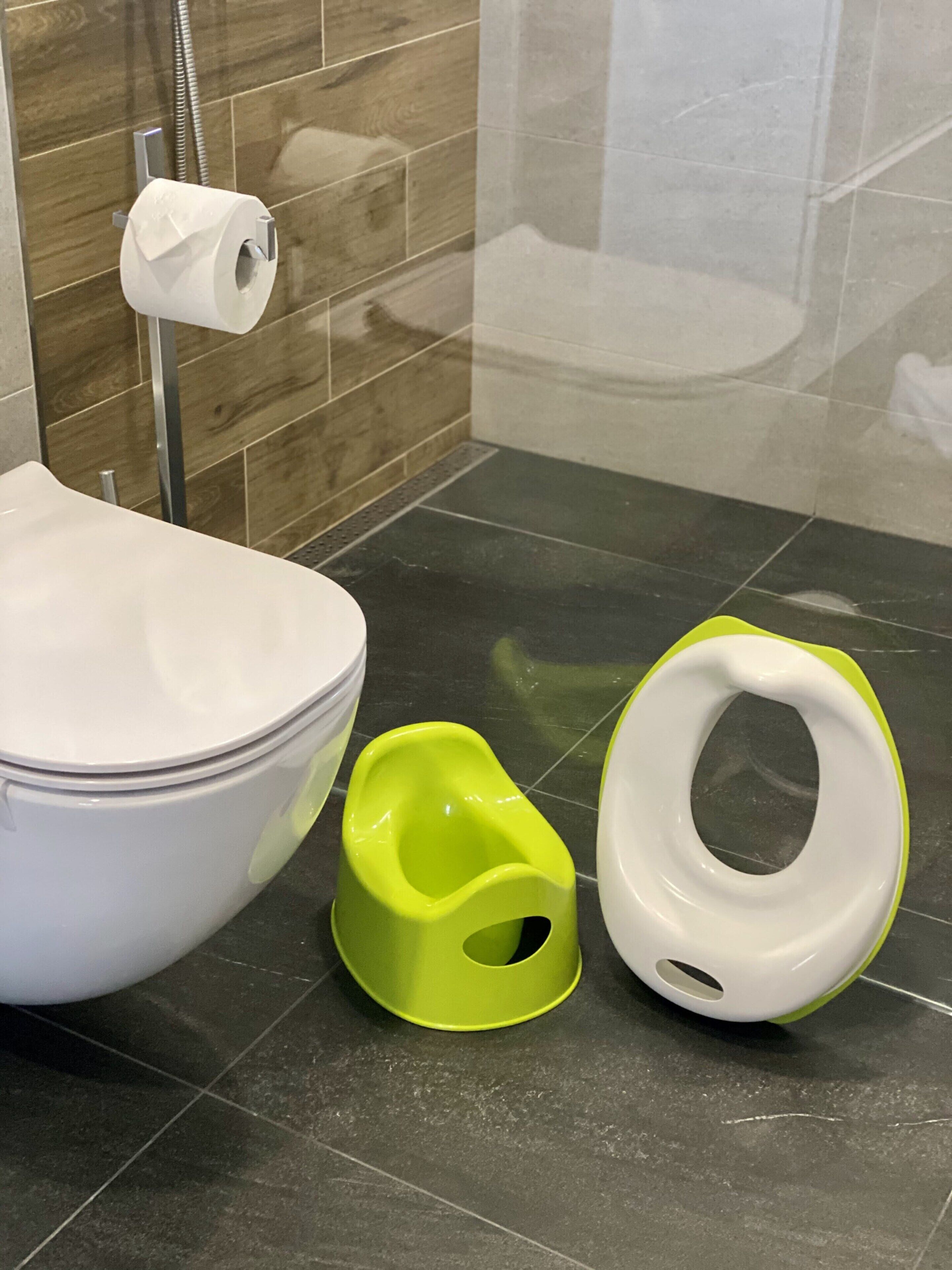 A bathroom with a toilet, a green and a white bidet, and a roll of toilet paper on the wall.