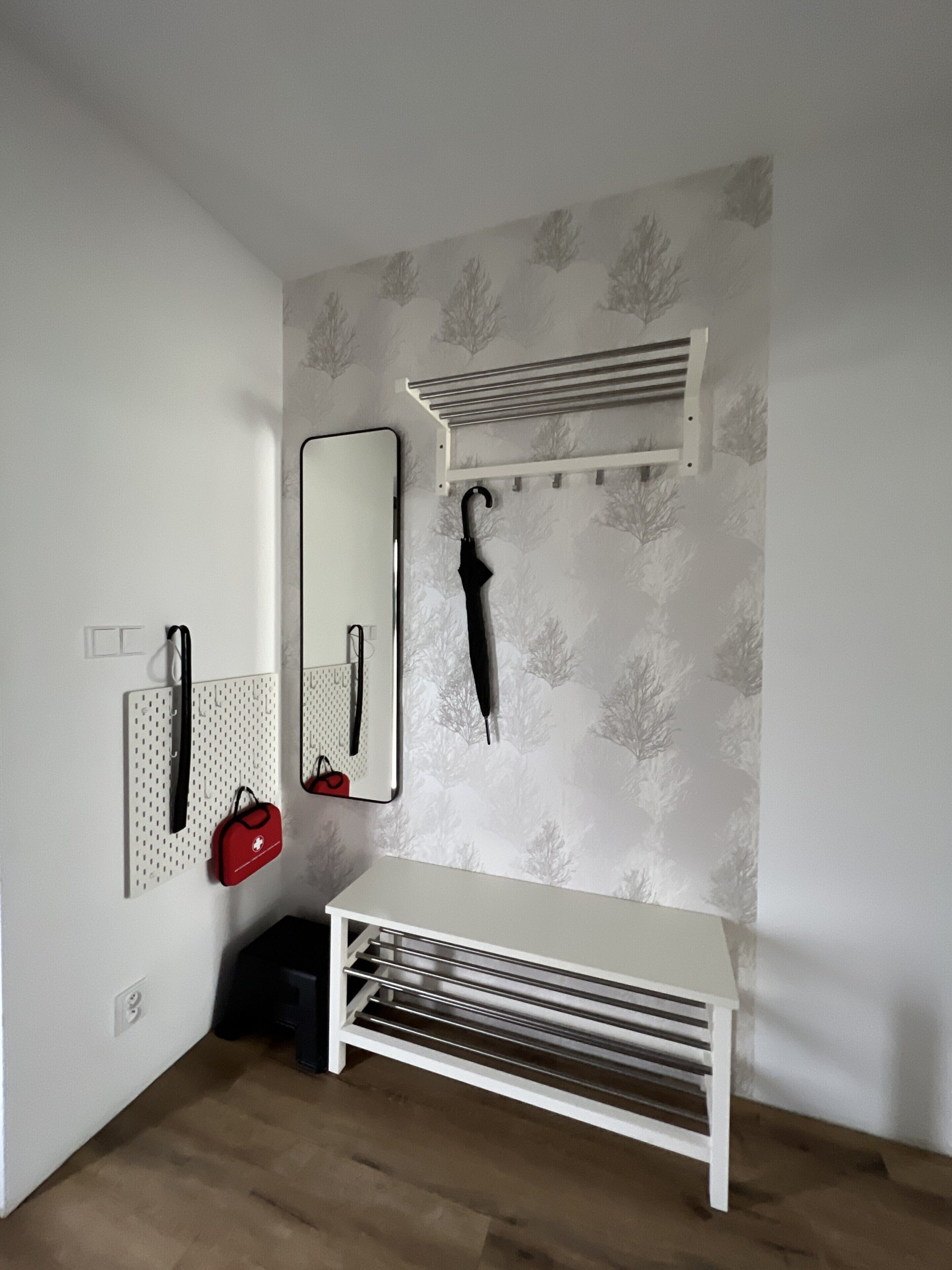 Una habitación con un banco blanco, un espejo fijado a la pared, un perchero y un radiador también sujeto a la pared.