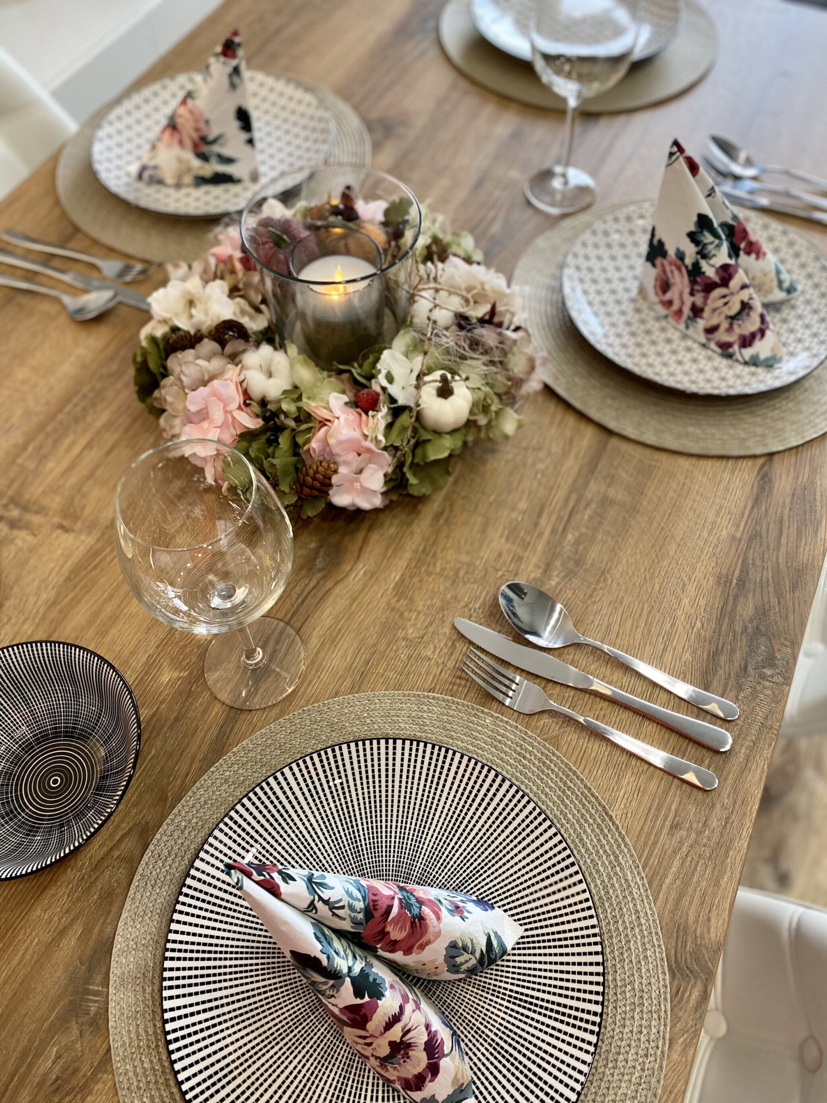 A wooden dining table with floral placemats, a candle centerpiece, and a glass of wine.