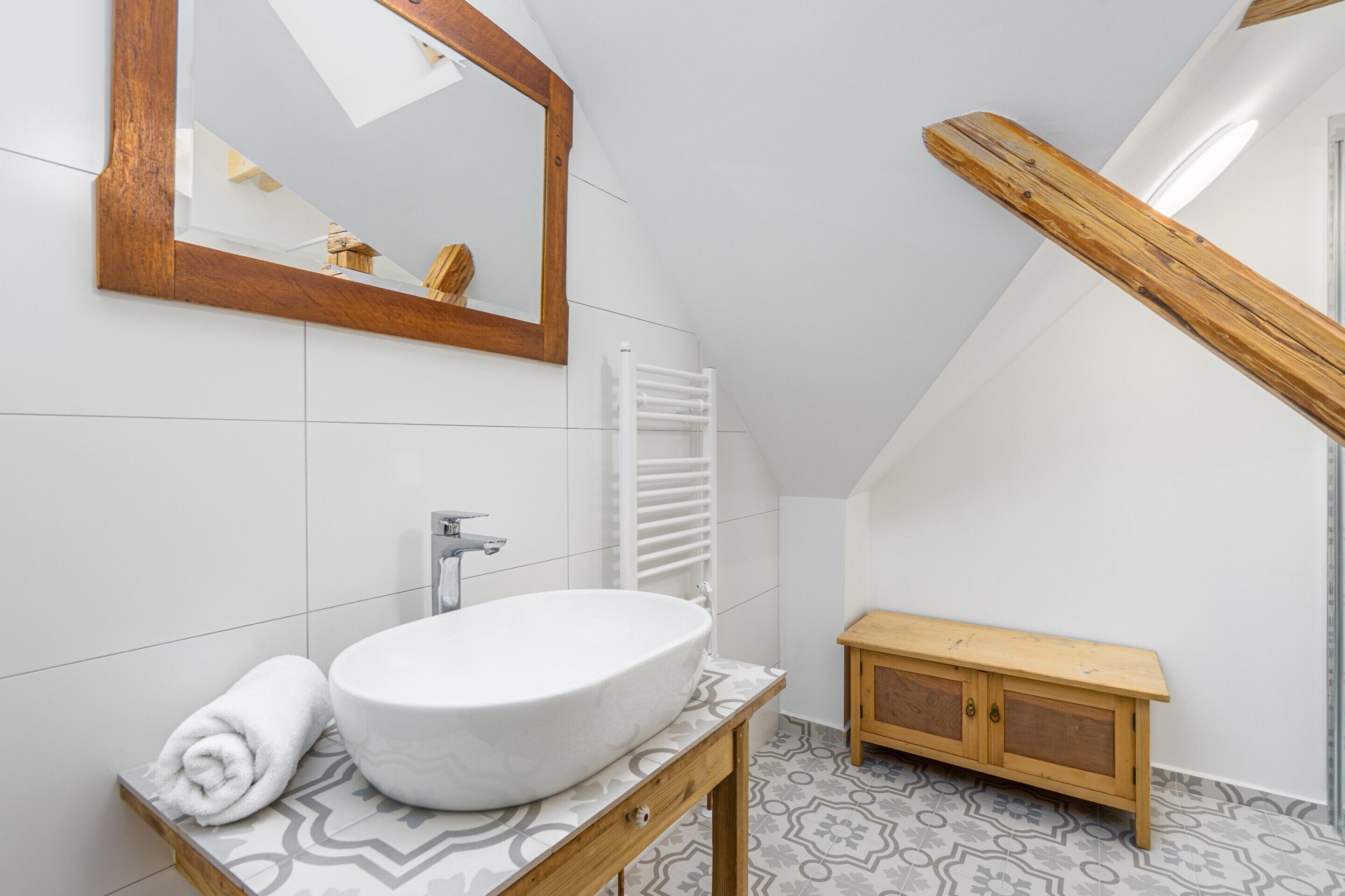 Un bagno moderno con un lavandino grande e bianco, un mobile contenitore in legno, un asciugamano bianco e uno specchio con cornice in legno.