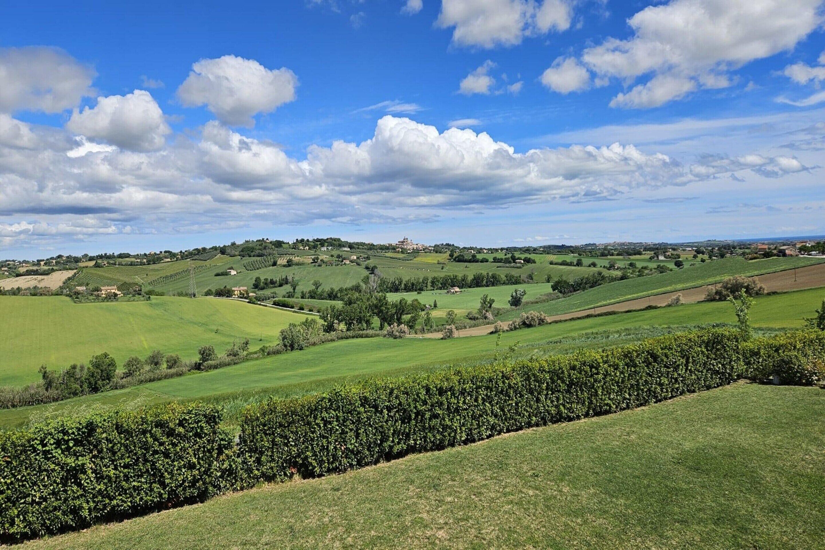 A panoramic view of a green landscape with rolling hills, a clear sky, and a distant building.