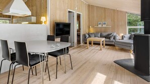 A modern cabin interior with a dining area, sofa, TV, and fireplace. - 5 Star Holiday Home in Saltum (Saltum)