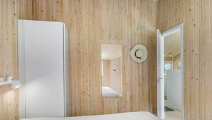 A bedroom with a wooden wall, a bed, a white door, and a mirror. - 5 Star Holiday Home in Saltum (Saltum)