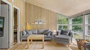 A modern living room with a wooden interior, a sofa set, a coffee table, and a large window providing a view of greenery. - 5 Star Holiday Home in Saltum (Saltum)
