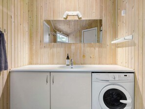 A bathroom with a wooden wall, a sink, a mirror, a washing machine, and a towel rack. - 5 Star Holiday Home in Saltum (Saltum)