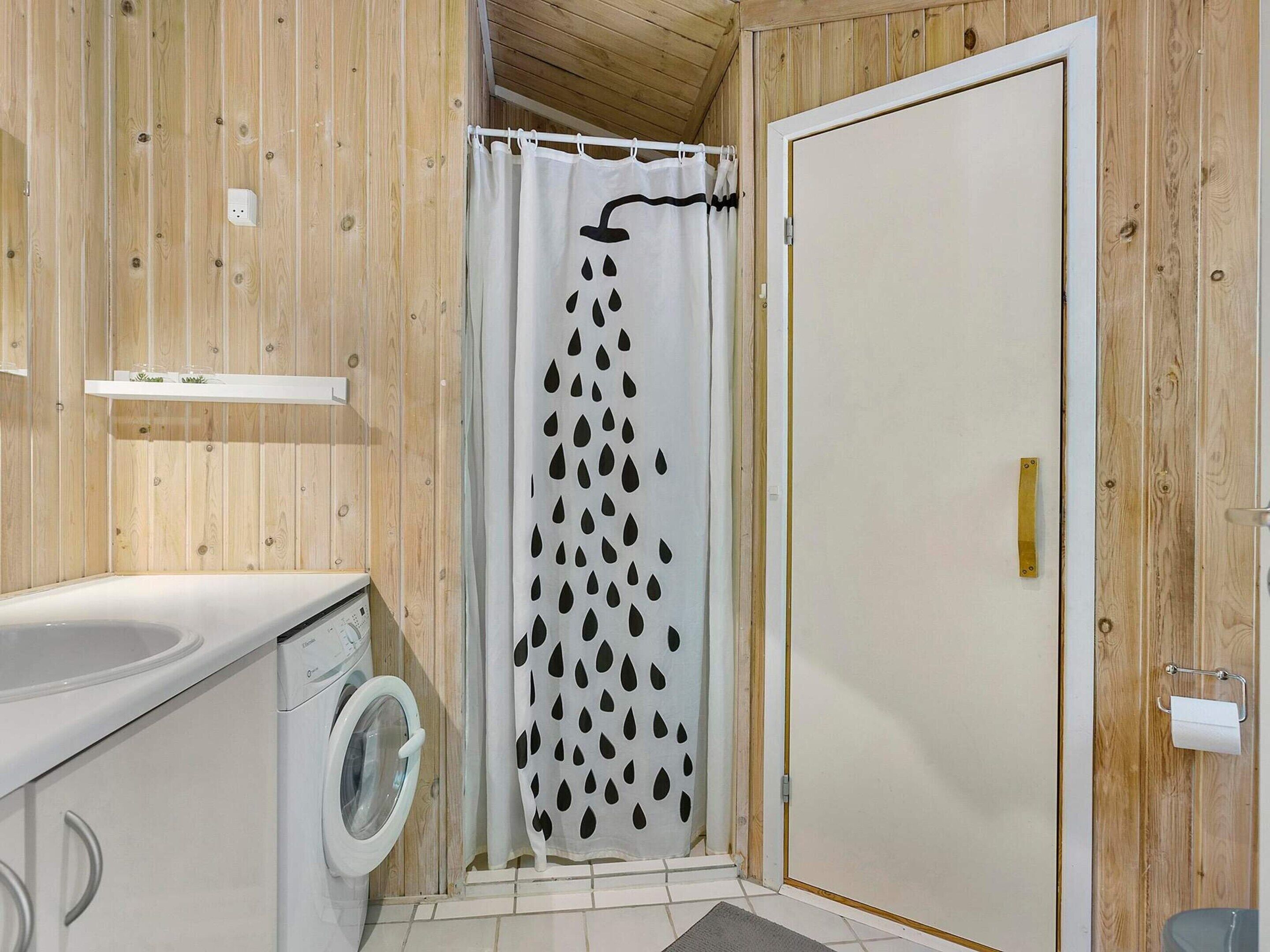 Ein Badezimmer mit Holzwänden, einer Waschmaschine, einem Duschvorhang mit Regenmuster und einem Toilettenpapierhalter.