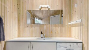 A compact bathroom with a wooden wall, a sink with a bottle of soap, a mirror, and a washing machine. - 5 Star Holiday Home in Saltum (Saltum)