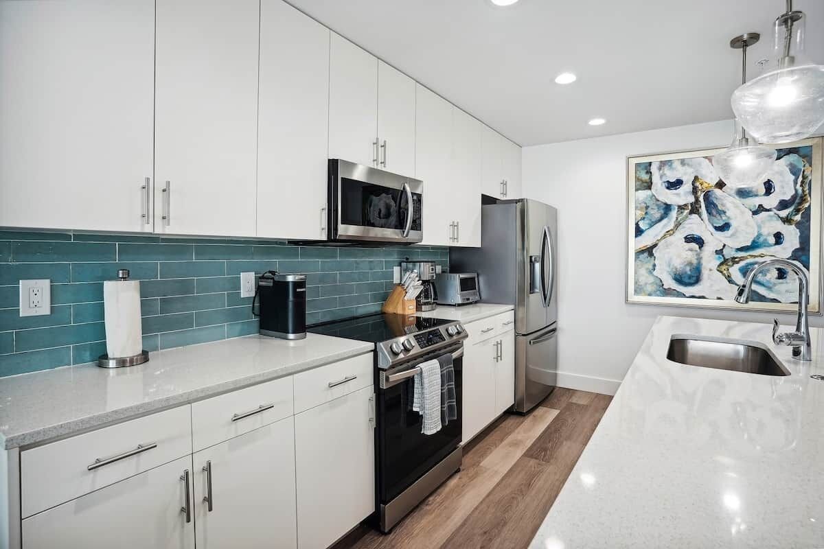 Una cocina moderna con armarios blancos, un microondas de acero inoxidable, una estufa, un refrigerador y un lavaplatos.