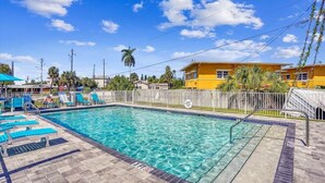 A rectangular swimming pool with clear blue water, surrounded by a tiled deck and a wooden fence. - Modern Coastal Condo - 4 Minute Walk to the Beach! (Madeira Beach)