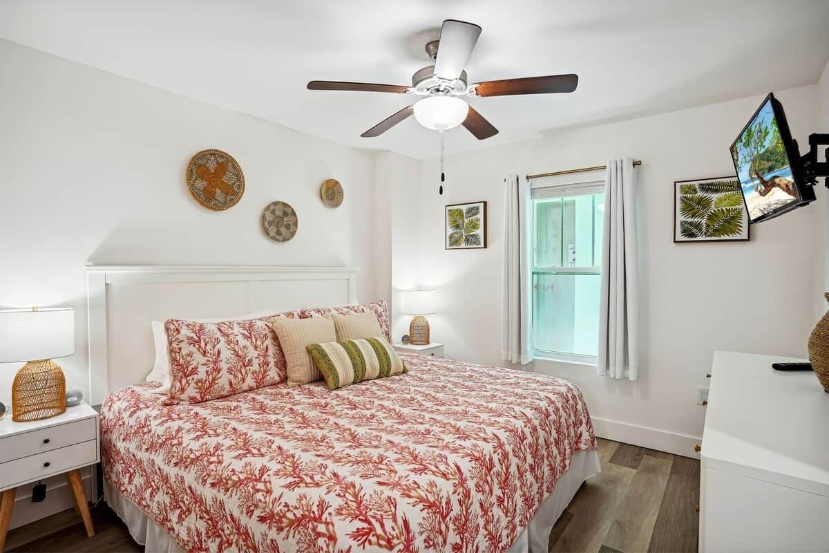 A bedroom with a bed, a ceiling fan, a window, and wall decorations.