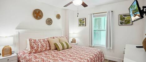 A bedroom with a bed, a ceiling fan, a window, and wall decorations.