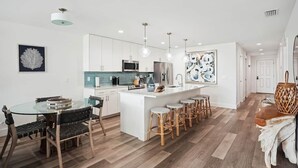 A modern kitchen with white cabinets, a central island with stools, and pendant lighting. - Modern Coastal Condo - 4 Minute Walk to the Beach! (Madeira Beach)