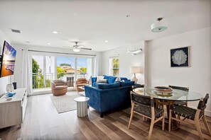 A modern living room with a blue sofa, glass dining table, and a ceiling fan.