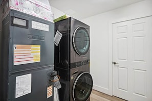 A stacked washer and dryer unit with visible labels and instructions, a white door, and a wooden floor. - Modern Coastal Condo-4 Minute Walk to the Beach (Madeira Beach)