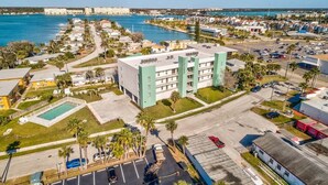 A coastal hotel with a swimming pool, parking lot, and a view of the sea. - Modern Coastal Condo - 4 Minute Walk to the Beach! (Madeira Beach)
