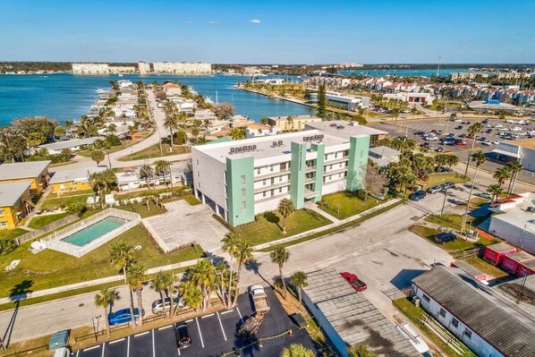 A coastal hotel with a swimming pool, parking lot, and a view of the sea. - Modern Coastal Condo - 4 Minute Walk to the Beach! (Madeira Beach)