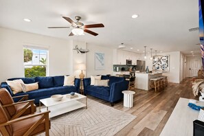 A spacious living area with a blue sofa set, a coffee table, and a dining area with stools.