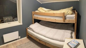 Una cama litera en una habitación con ventana, un radiador y una pequeña mesa con un libro.
