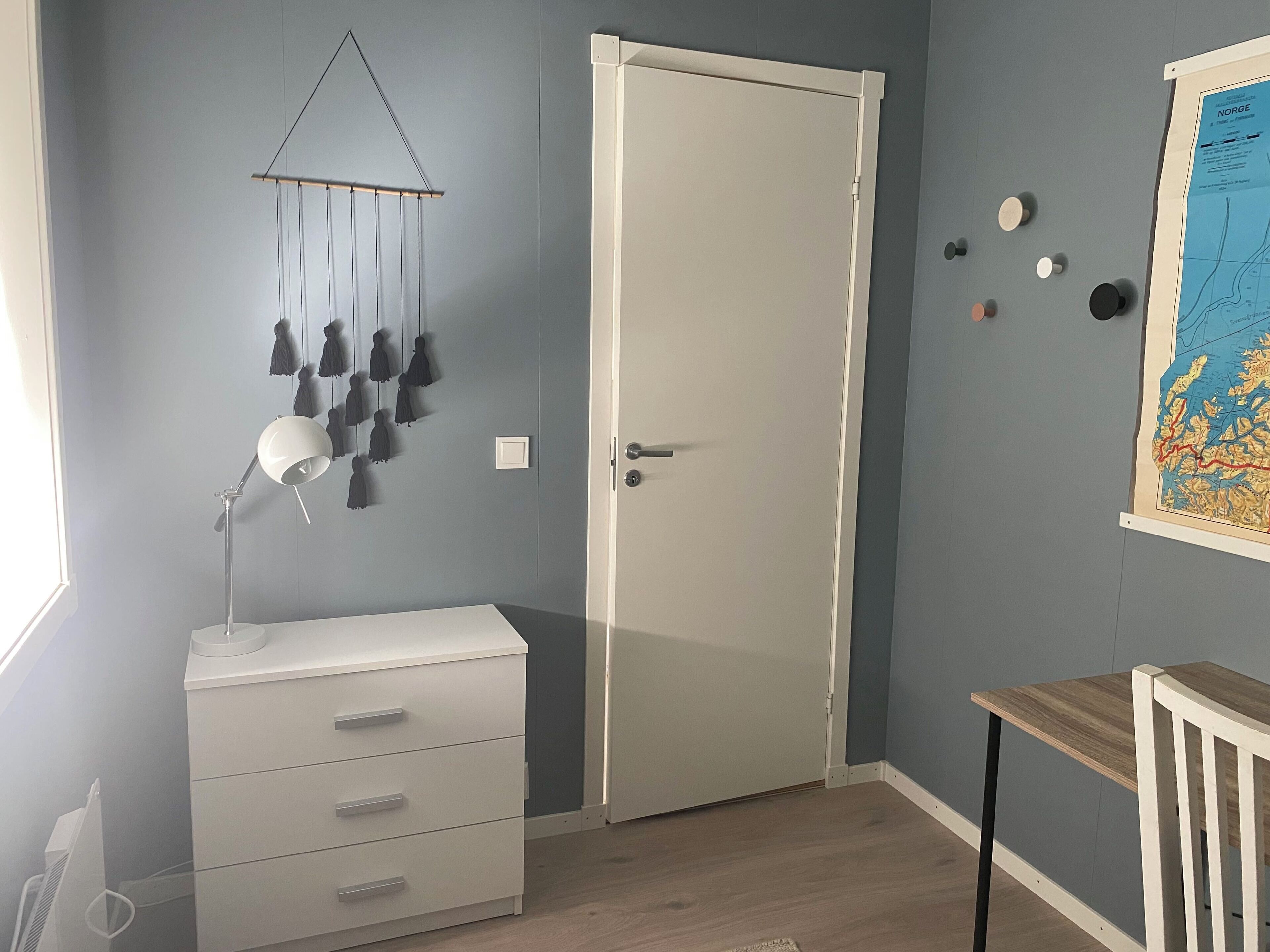 A room with a white dresser, a door, a hanging light fixture, and a map on the wall.