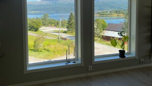 Una habitación con ventanas amplias que ofrecen vista a un lago, montañas y una carretera.