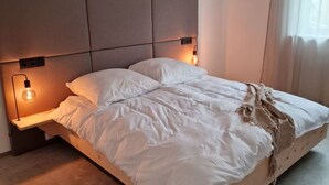 A modern bedroom with a large bed, two bedside lamps, and a headboard with built-in lighting. - Barrier-free enjoyment in Unterallgäu, modern apartment with style and comfort   (Oberschönegg)