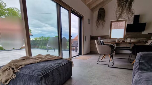 A spacious living area with a large sliding glass door leading to an outdoor patio, a comfortable seating area with a sofa and chairs, and a dining setup with a table and chairs. - Barrier-free enjoyment in Unterallgäu, modern apartment with style and comfort   (Oberschönegg)