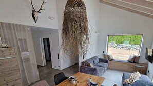 A modern living room with a wooden dining table set for four, a sofa, and a large window offering a view of greenery. - Barrier-free enjoyment in Unterallgäu, modern apartment with style and comfort   (Oberschönegg)