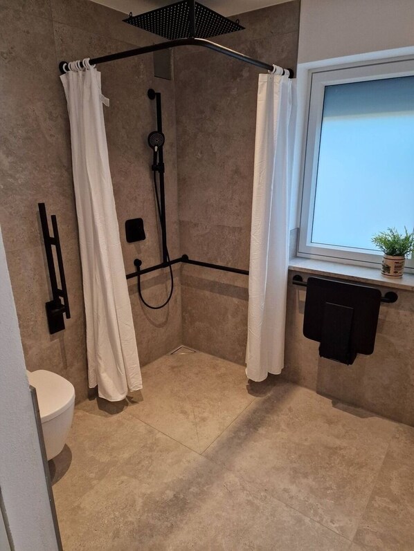 Moderni kylpyhuone, jossa on suihkutila, wc ja ikkuna, jonka edessä on kasvi.
