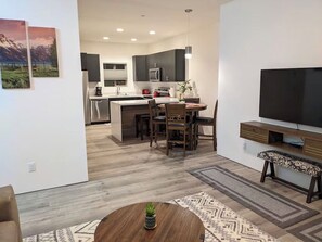 Une cuisine moderne avec des meubles de couleur sombre, un îlot central et un coin repas doté de chaises en bois.