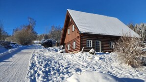 Une cabane en bois avec un toit en pente, entourée d’un paysage enneigé et d’arbres.