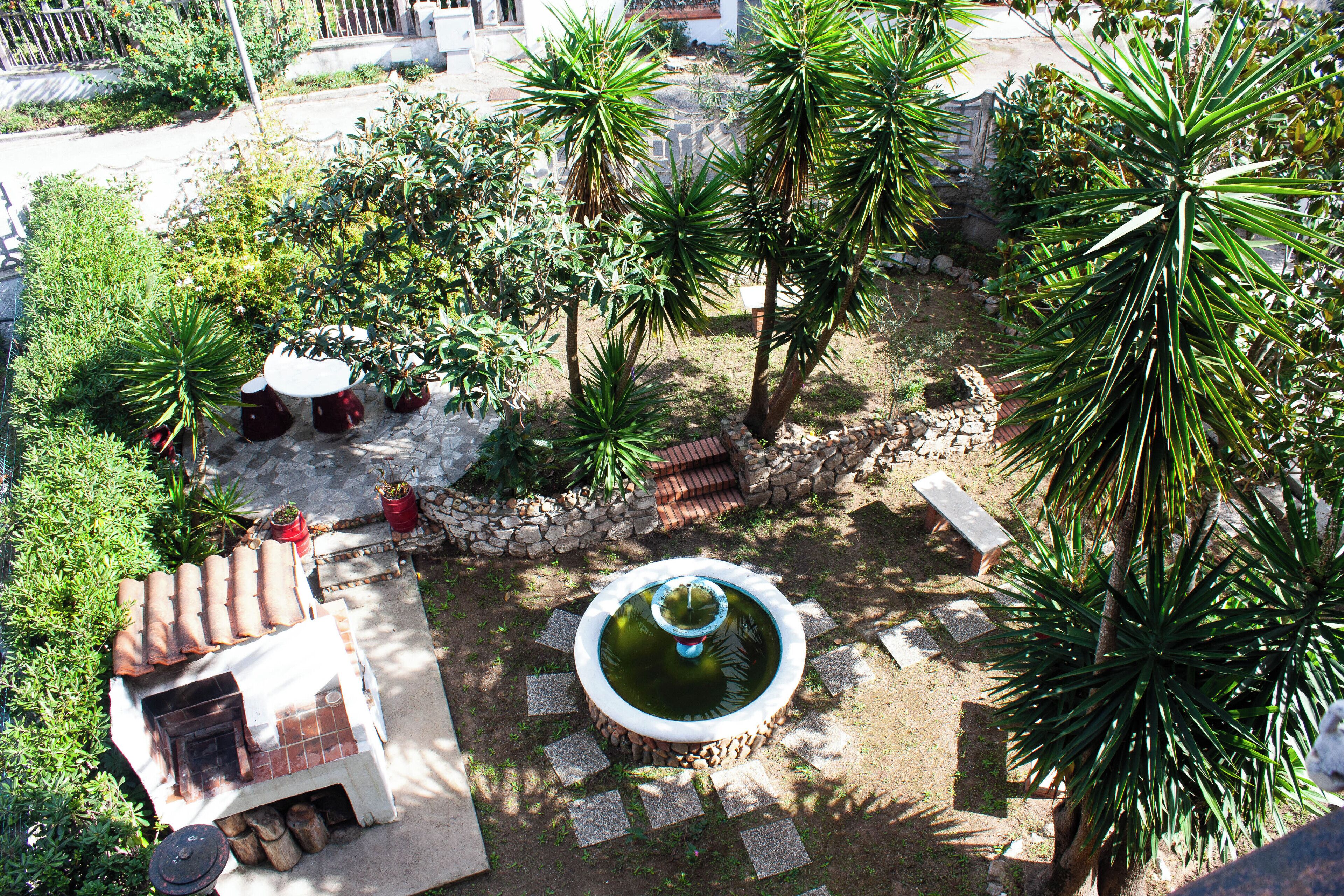 Un patio con una pequeña fuente, plantas en macetas y una zona de patio con baldosas.