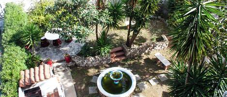 A courtyard with a small fountain, potted plants, and a tiled patio area.