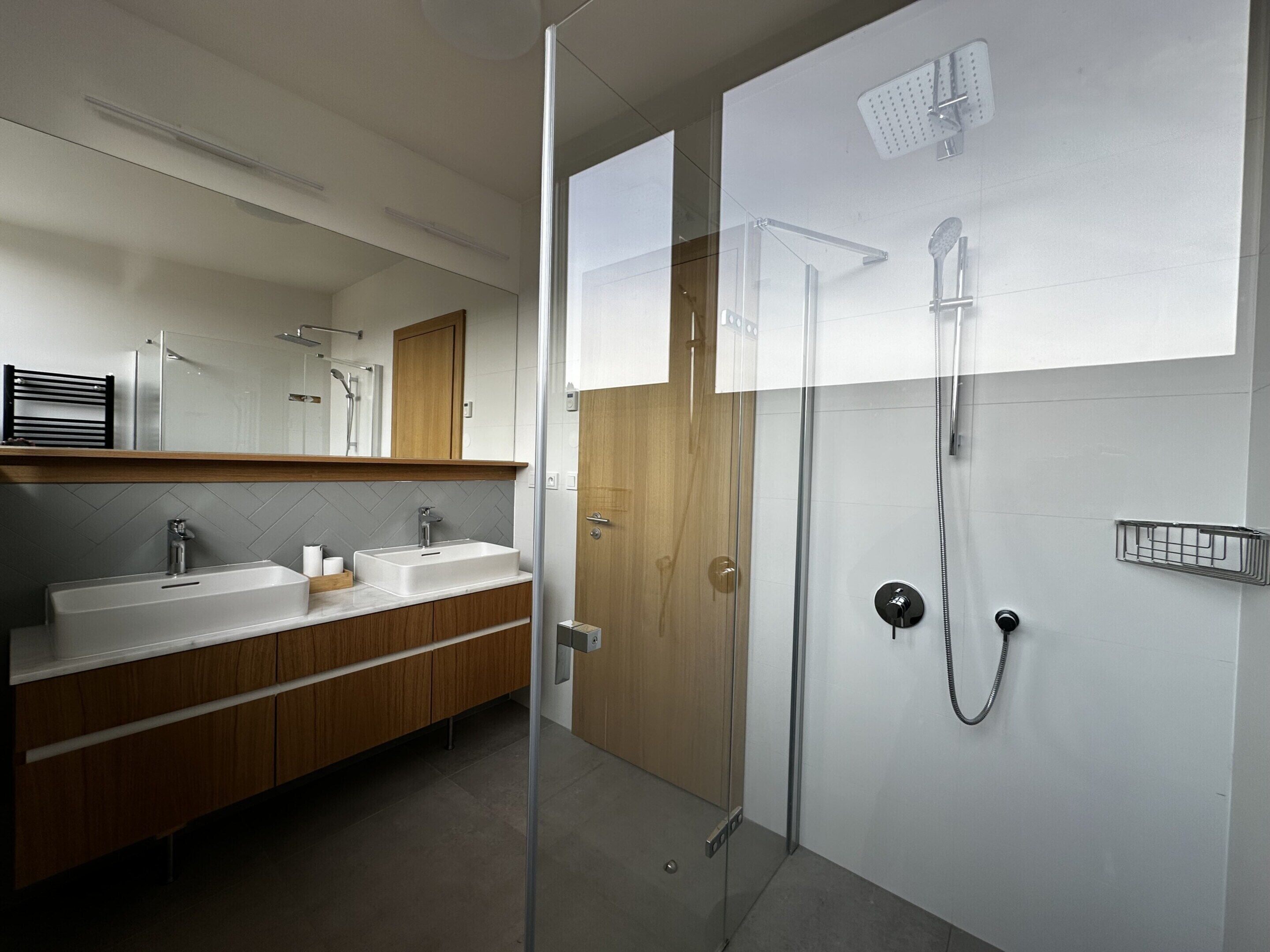 A modern bathroom with a glass-enclosed shower, a double sink vanity, and a wooden door.