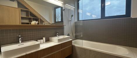A modern bathroom with two sinks, a bathtub, wooden cabinets, and a large window.