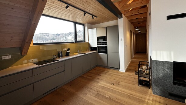 Une cuisine moderne avec des poutres en bois, une grande fenêtre et des appareils électroménagers intégrés.