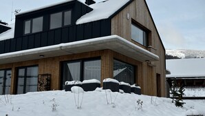 Une maison moderne à deux étages, dotée d’un toit en pente recouvert de neige, de grandes fenêtres et de fondations en pierre.