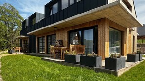 Une maison moderne à deux étages, dotée d’un patio couvert, de grandes fenêtres et d’une pelouse bien entretenue.