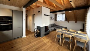 Une cuisine moderne dotée d’appareils électroménagers intégrés, un coin repas avec une table et des chaises en bois, et un espace de vie chaleureux agrémenté d’une cheminée.