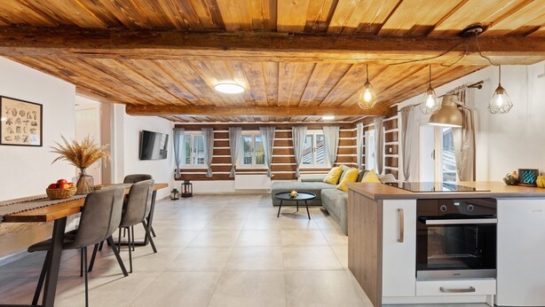 A spacious kitchen with a wooden ceiling, a dining area with chairs and a table, and a sofa in the background.