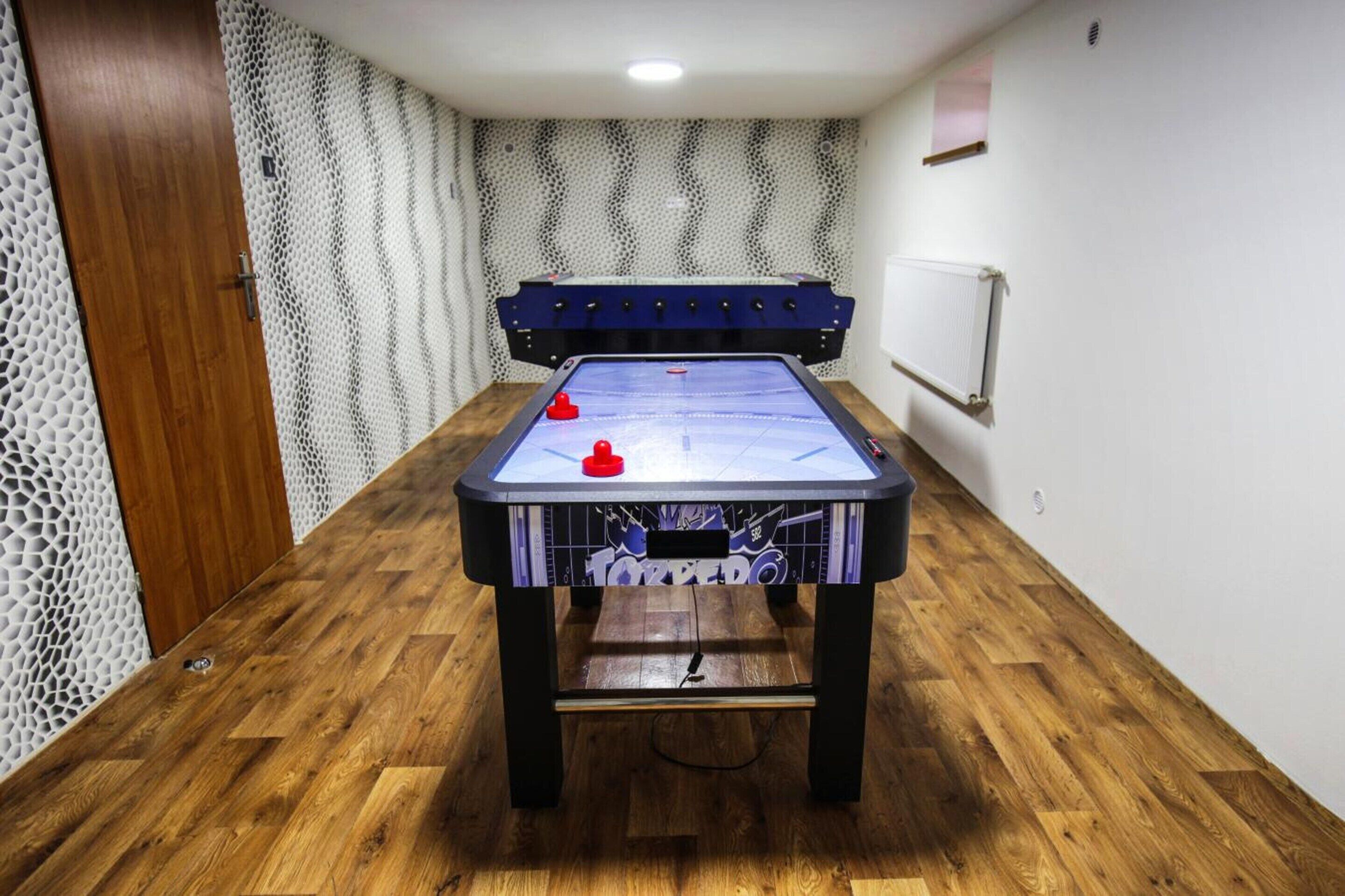 Une pièce avec une table de baby-foot, un plancher en bois, un mur décoré d’un motif et un tableau blanc accroché au mur.