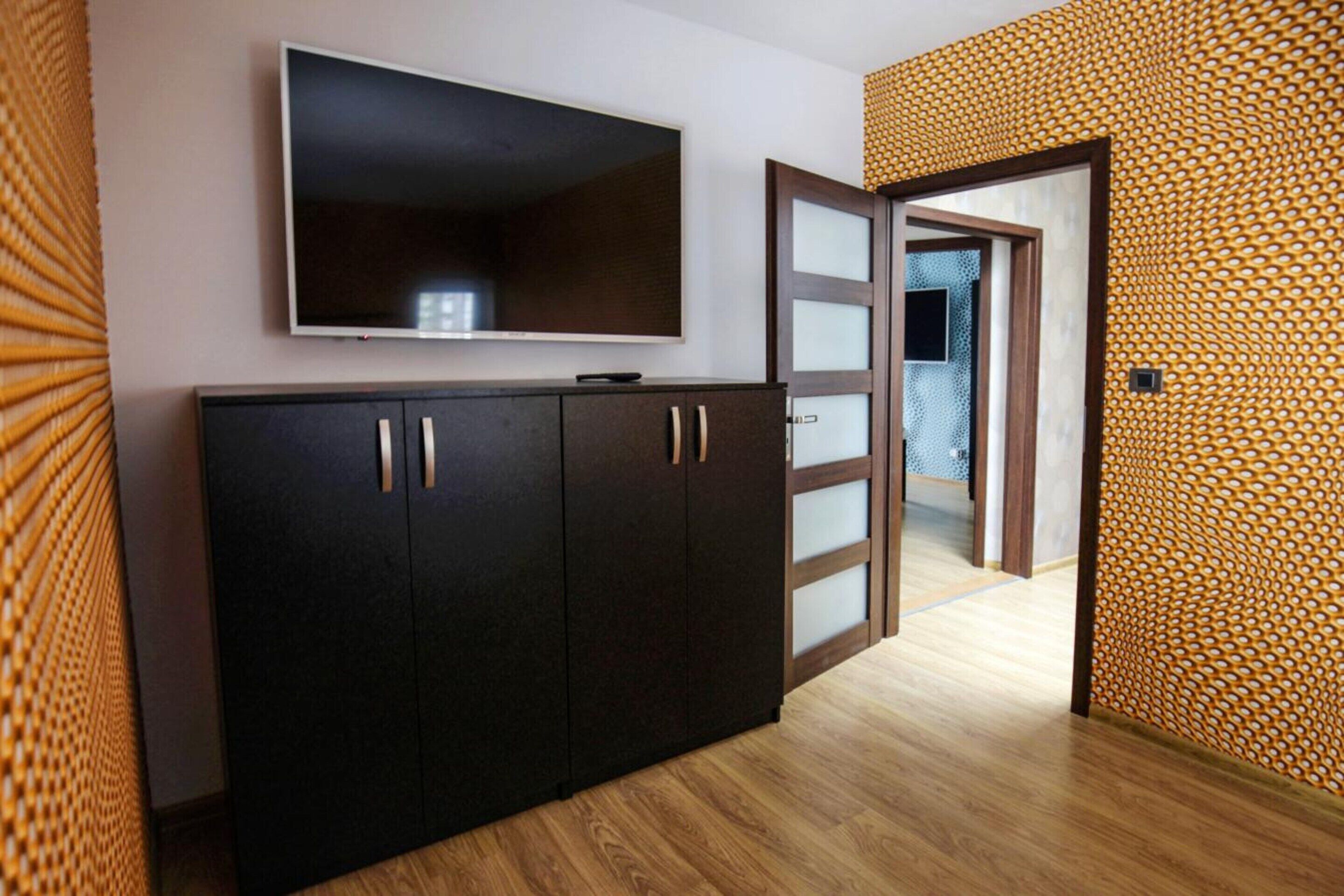 A room with a dark wooden cabinet, a flat-screen TV mounted above it, and a patterned wall.
