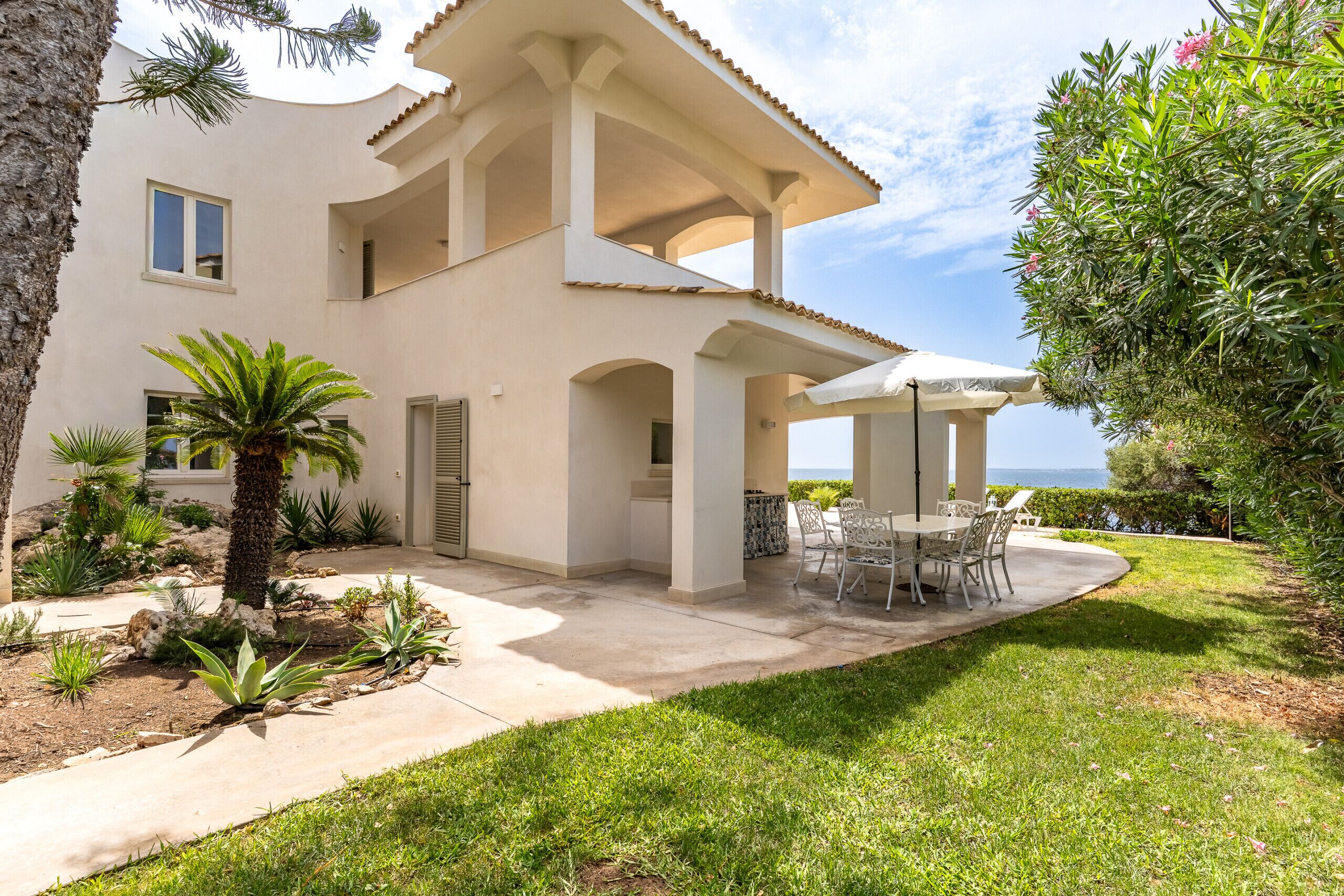 A two-story house with a covered patio, outdoor furniture, and a view of the sea.