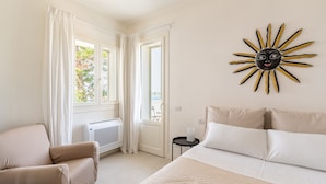 Ein Schlafzimmer mit einem Bett, einem Sessel, einer Wanddekoration in Sonnenform und einem Fenster mit Vorhängen.