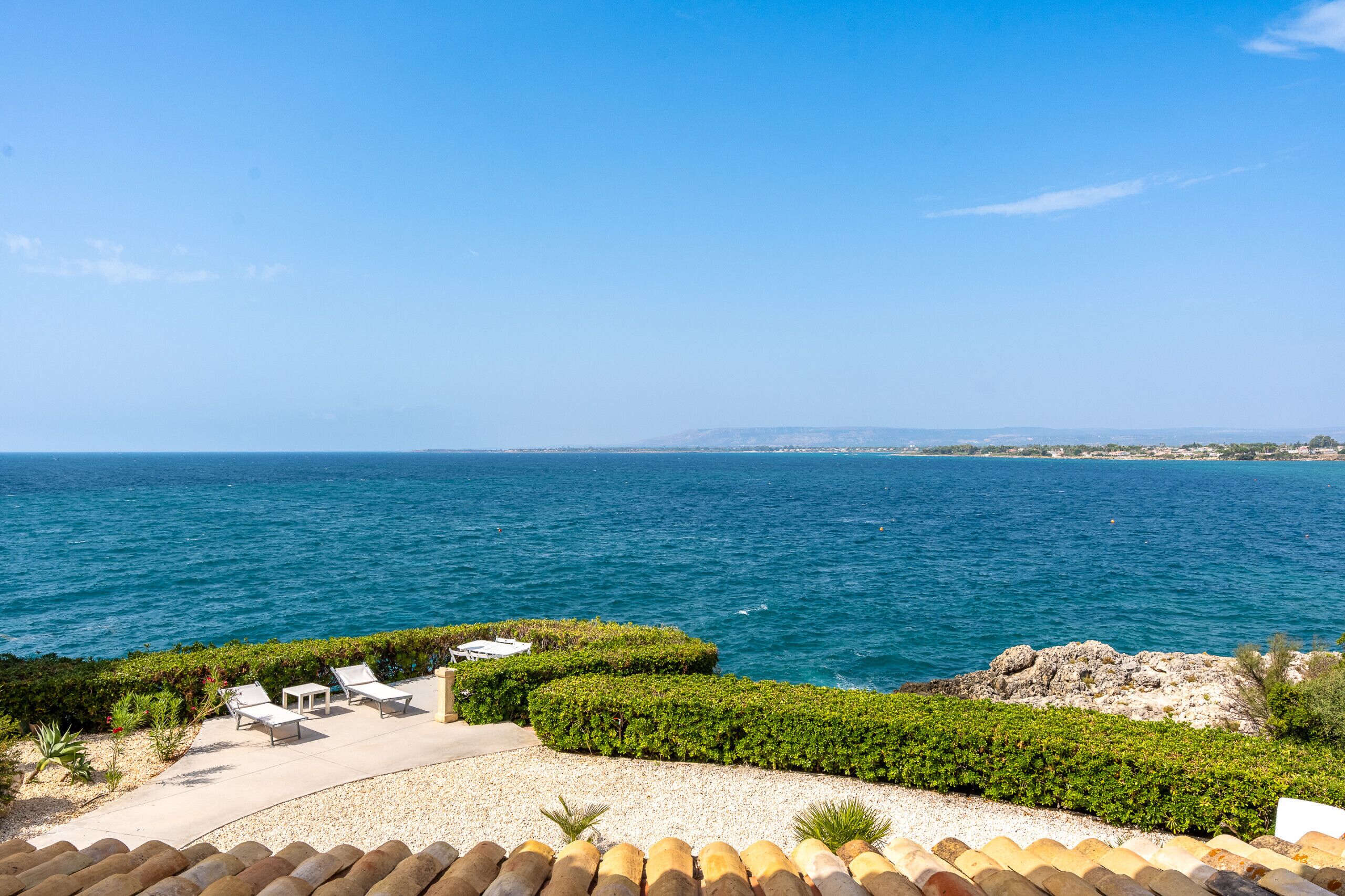 A coastal view with a patio area, seating, and a view of the sea.