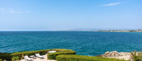 A coastal view with a patio area, seating, and a view of the sea.