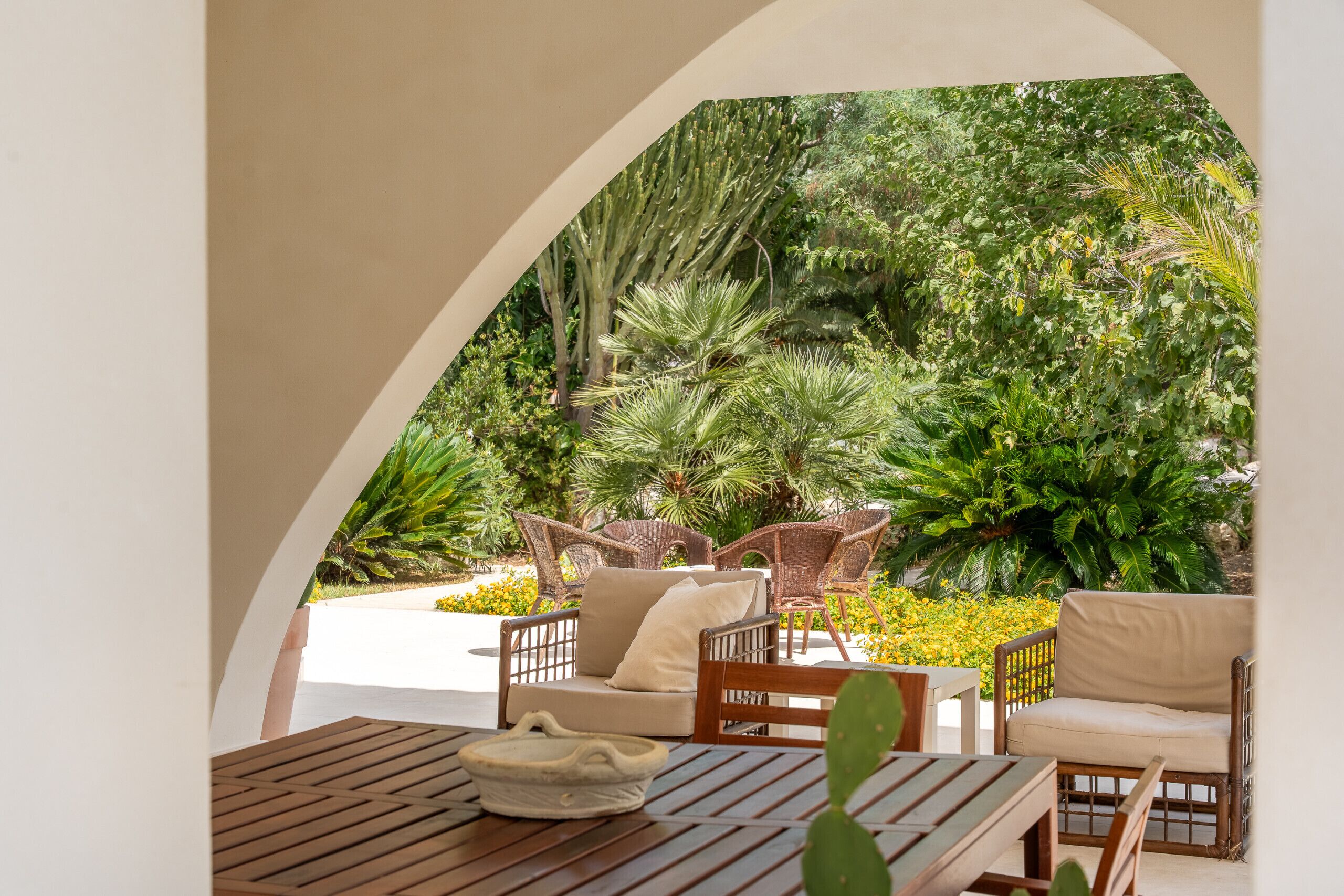 An outdoor seating area with wicker furniture, a wooden table, and a view of lush greenery.